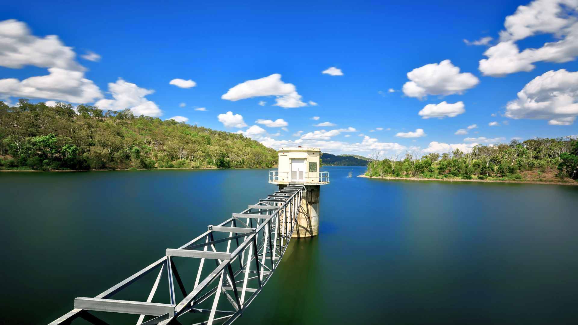 Water intake tower rising from Cooby Dam against forested hills.