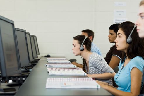 people (assume learning) with papers sitting in front of a line of computer screens on a desk