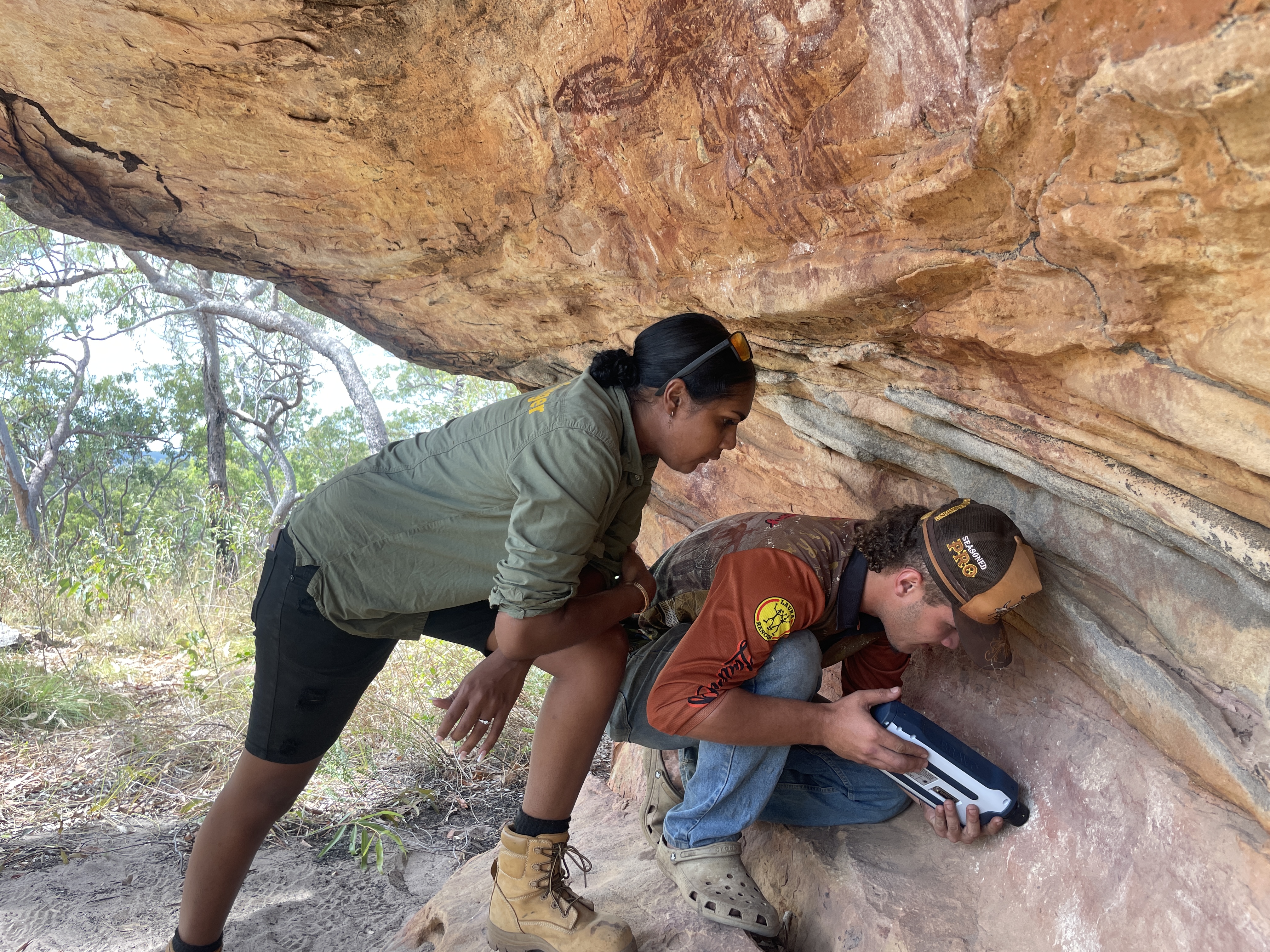 Two rangers use scientific equipment on rock art in rock shelter