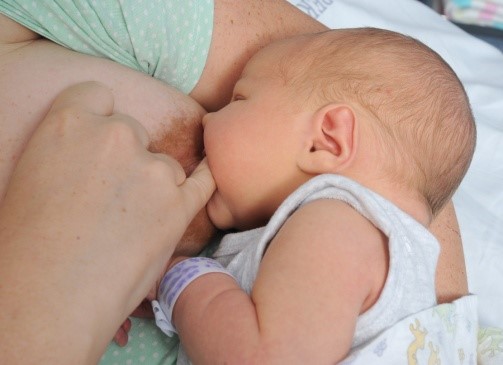 Baby breastfeeding, mother has her little finger in the corner of the baby&rsquo;s mouth.