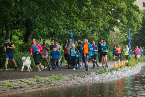 group of people and dogs running together along a waterside road
