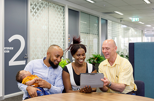 Young family with consultant sitting around a table outdoors looking at a tablet.